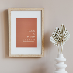 Red brown print reading 'take a deep Breath' in a light frame on a beige wall